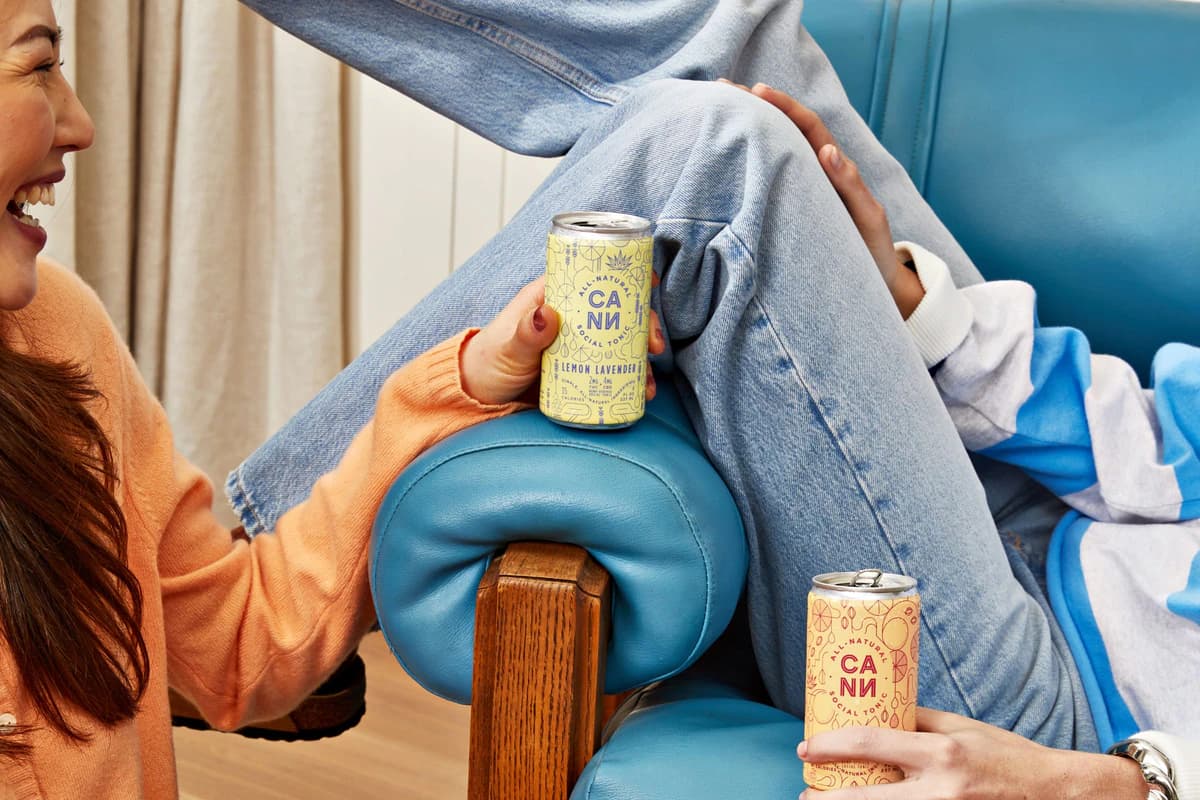 Two people holding Cann cans beside a blue armchair